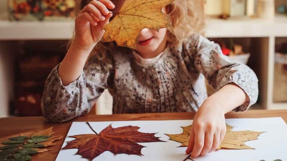 Kind bastelt mit Herbstblätter auf Papier.
